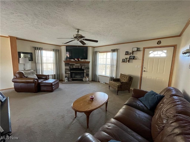 carpeted living area with a stone fireplace, crown molding, plenty of natural light, and a ceiling fan