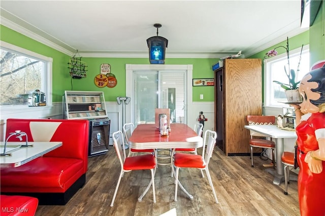 dining space with a wealth of natural light, a wainscoted wall, wood finished floors, and ornamental molding