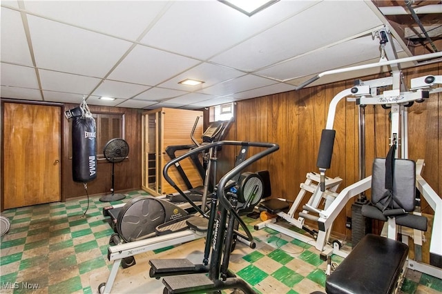 exercise area with tile patterned floors, a paneled ceiling, and wood walls