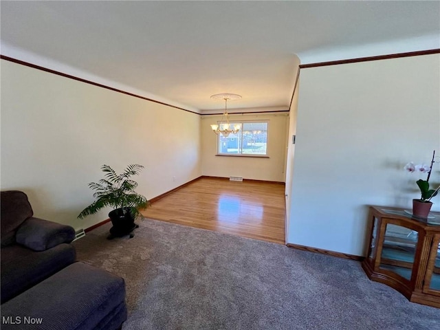 unfurnished living room with a notable chandelier, ornamental molding, wood finished floors, carpet flooring, and baseboards