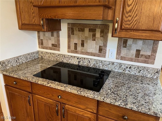 kitchen with brown cabinetry, light stone counters, tasteful backsplash, and black electric cooktop