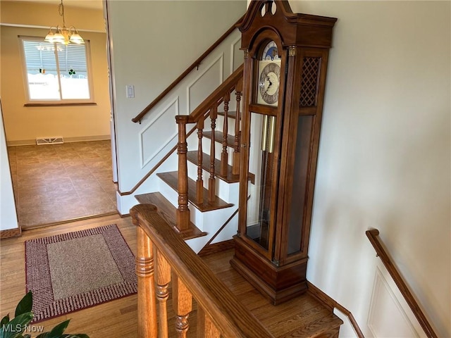 stairs with visible vents, baseboards, an inviting chandelier, and wood finished floors