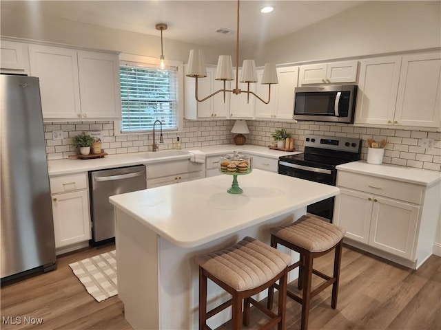 kitchen with stainless steel appliances, a kitchen bar, decorative backsplash, and white cabinetry