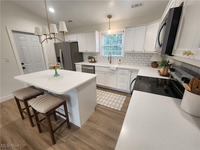 kitchen featuring a sink, a kitchen island, backsplash, wood finished floors, and stainless steel appliances