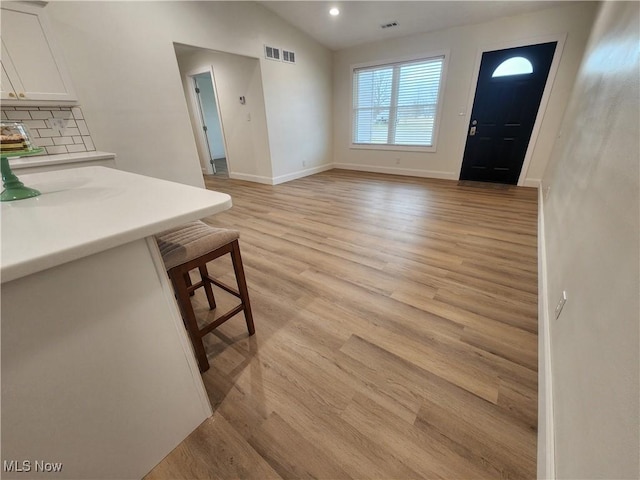 interior space with visible vents, baseboards, light wood-style floors, and vaulted ceiling