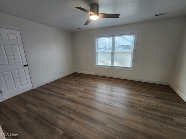 empty room with dark wood finished floors, visible vents, a ceiling fan, and baseboards