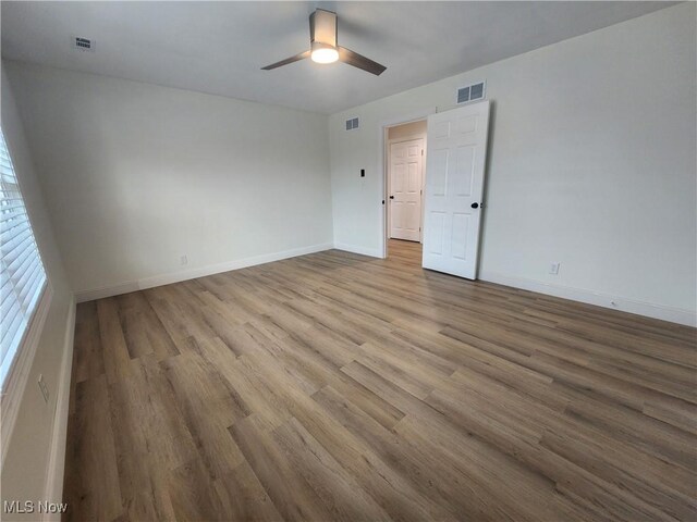 empty room featuring wood finished floors, a ceiling fan, visible vents, and baseboards