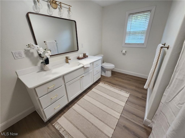 bathroom with toilet, vanity, baseboards, and wood finished floors