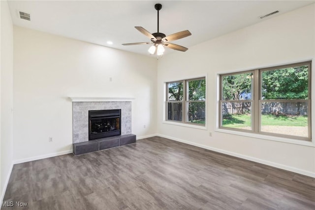 unfurnished living room with visible vents, a ceiling fan, a tiled fireplace, wood finished floors, and baseboards