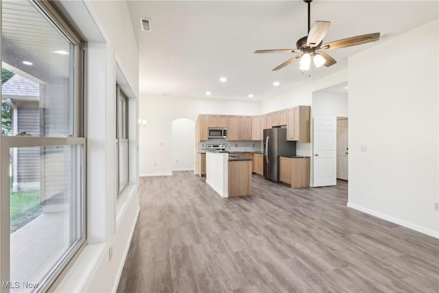 kitchen featuring visible vents, a kitchen island with sink, light brown cabinets, stainless steel appliances, and arched walkways