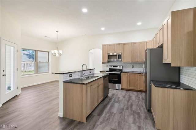 kitchen featuring a kitchen island with sink, a sink, dark countertops, appliances with stainless steel finishes, and a chandelier