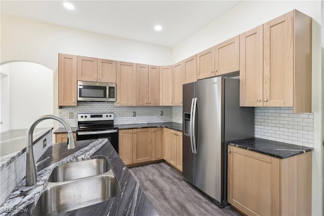 kitchen with light brown cabinets, a sink, tasteful backsplash, wood finished floors, and appliances with stainless steel finishes