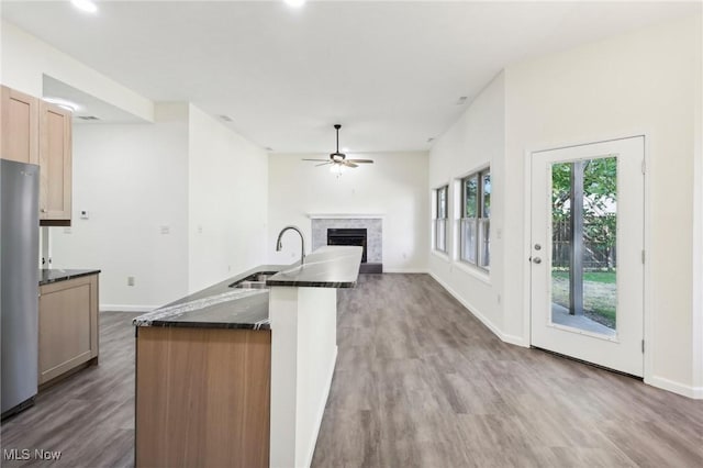 kitchen with a ceiling fan, wood finished floors, a fireplace, freestanding refrigerator, and a sink