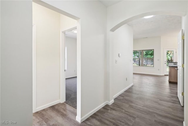 hallway featuring arched walkways, dark wood finished floors, and baseboards