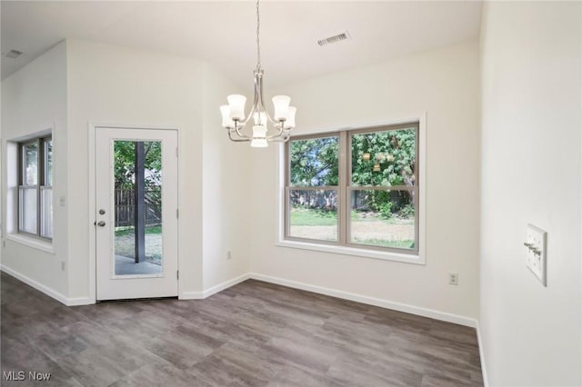 unfurnished dining area featuring dark wood-type flooring, baseboards, visible vents, and a chandelier