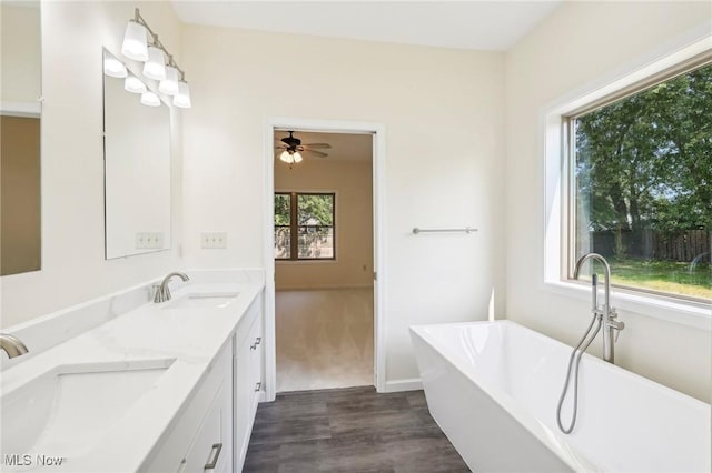 full bathroom with double vanity, wood finished floors, a freestanding bath, and a sink