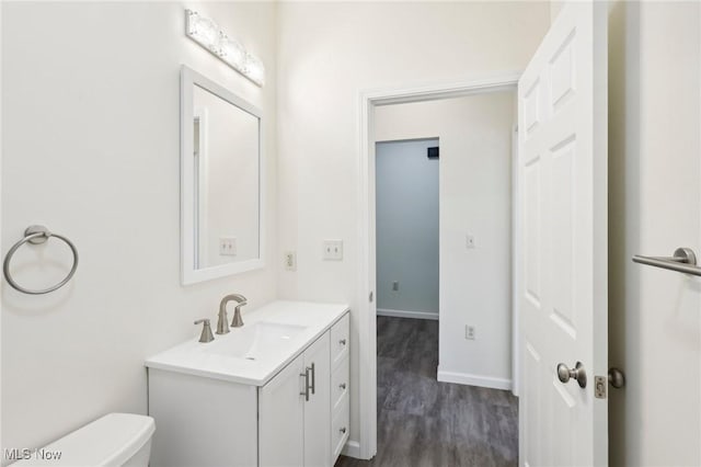 bathroom with baseboards, toilet, wood finished floors, and vanity