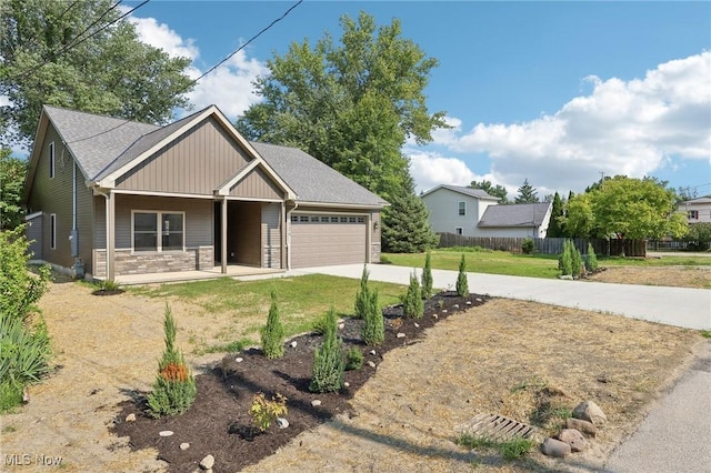 view of front of home featuring a front lawn, driveway, stone siding, fence, and a garage