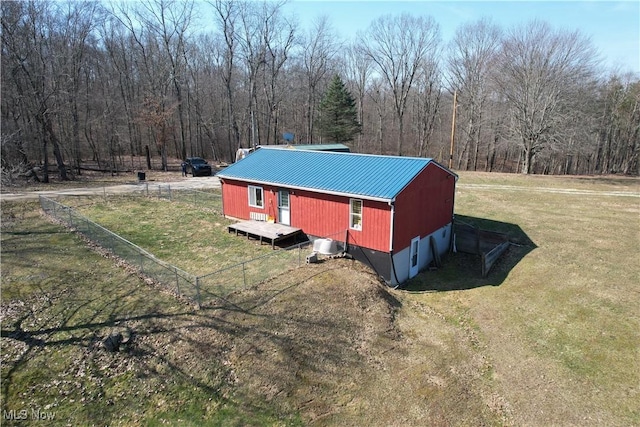 exterior space with fence, a lawn, a forest view, and metal roof