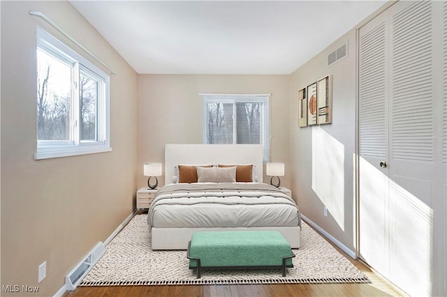 bedroom with wood finished floors, visible vents, a closet, and baseboards