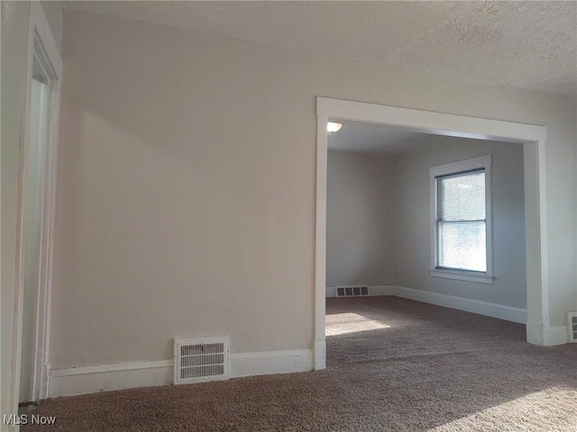 carpeted spare room featuring baseboards, visible vents, and a textured ceiling