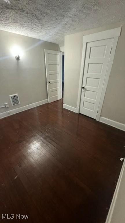 empty room featuring visible vents, baseboards, a textured ceiling, and dark wood-style floors