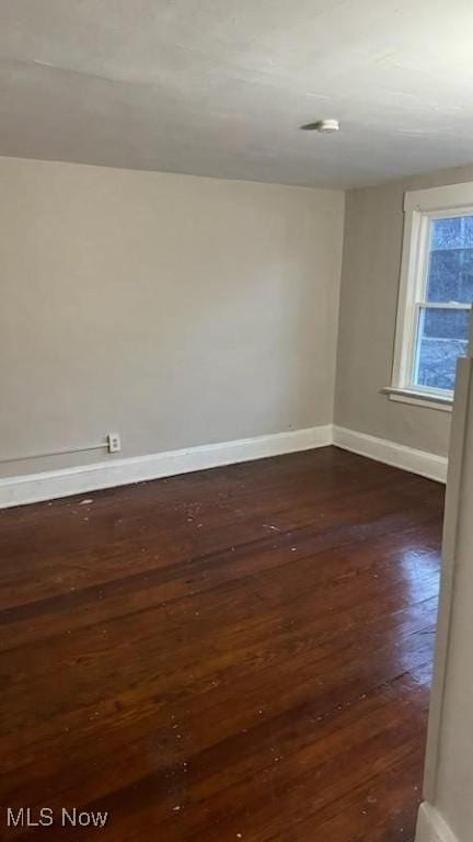 spare room with baseboards and dark wood-style flooring