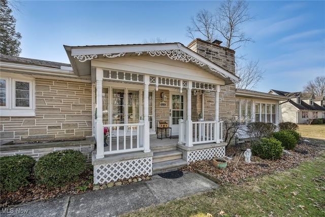 view of front of home featuring stone siding, covered porch, and a chimney