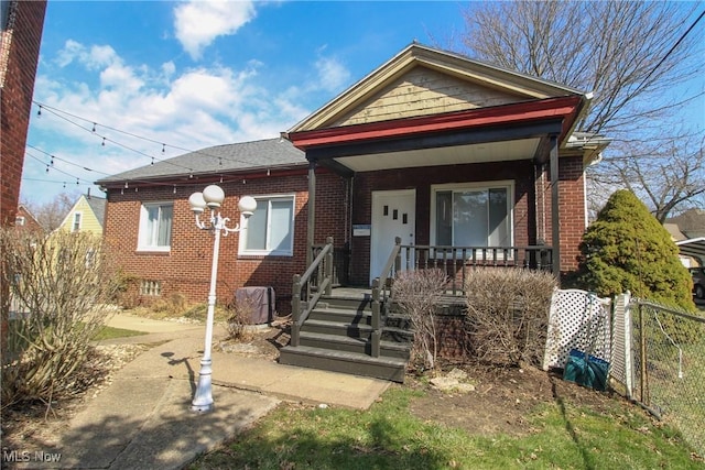 bungalow-style home featuring brick siding, a porch, and fence