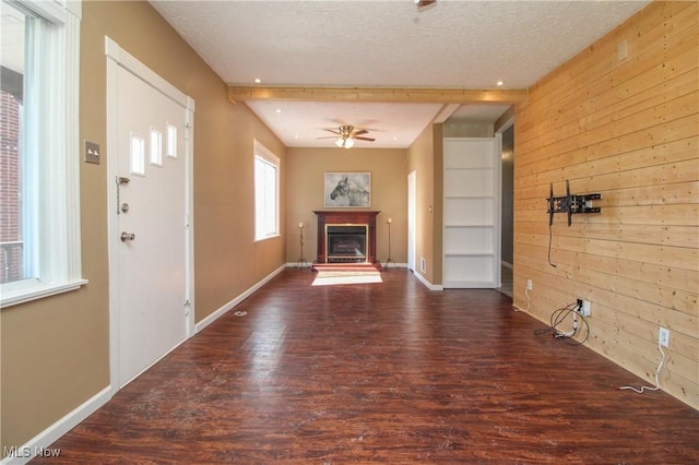 unfurnished living room featuring wooden walls, a glass covered fireplace, ceiling fan, and wood finished floors