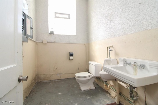 bathroom with toilet, unfinished concrete flooring, and a sink