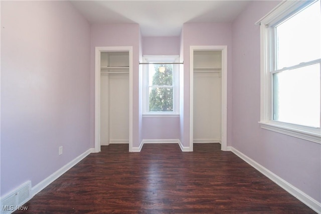 unfurnished bedroom featuring visible vents, baseboards, two closets, and dark wood-type flooring