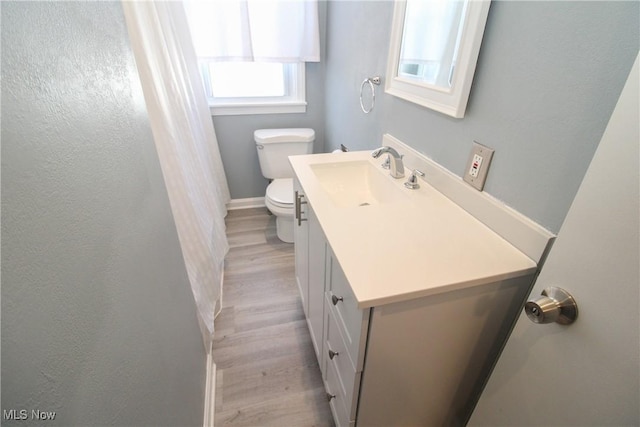 bathroom featuring baseboards, toilet, wood finished floors, and vanity