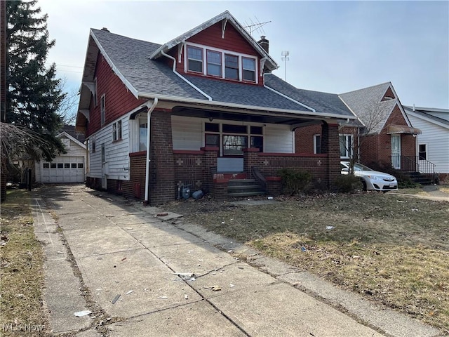 bungalow-style home with an outbuilding, brick siding, covered porch, and a shingled roof