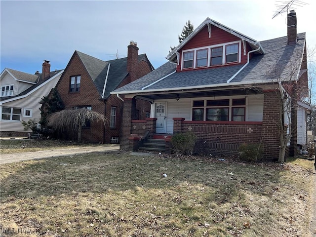 bungalow-style home with brick siding, a porch, a chimney, and a front yard