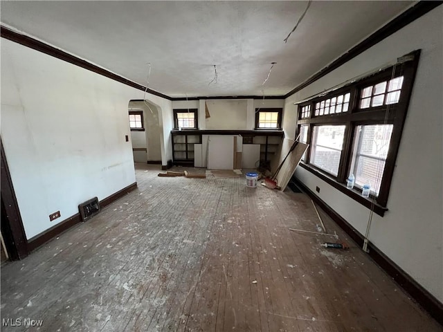 unfurnished living room featuring arched walkways, crown molding, baseboards, and hardwood / wood-style floors