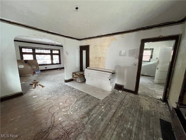 unfurnished living room with arched walkways, crown molding, baseboards, and wood-type flooring