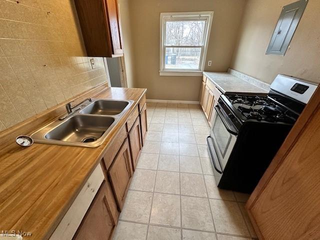 kitchen with stainless steel gas range oven, a sink, tasteful backsplash, light tile patterned flooring, and baseboards