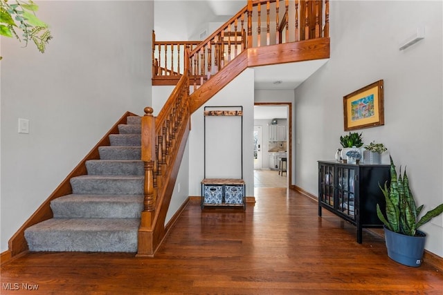 staircase featuring baseboards, wood finished floors, and a towering ceiling