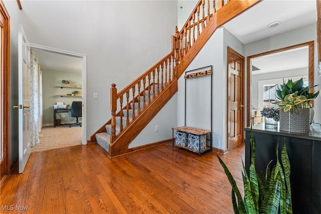 staircase with baseboards, wood finished floors, and a towering ceiling