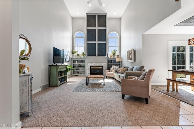 living room with visible vents, baseboards, a high ceiling, and a glass covered fireplace