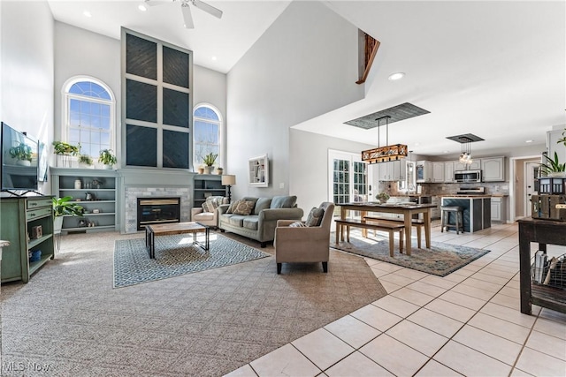 living room featuring a glass covered fireplace, recessed lighting, a high ceiling, light tile patterned flooring, and ceiling fan