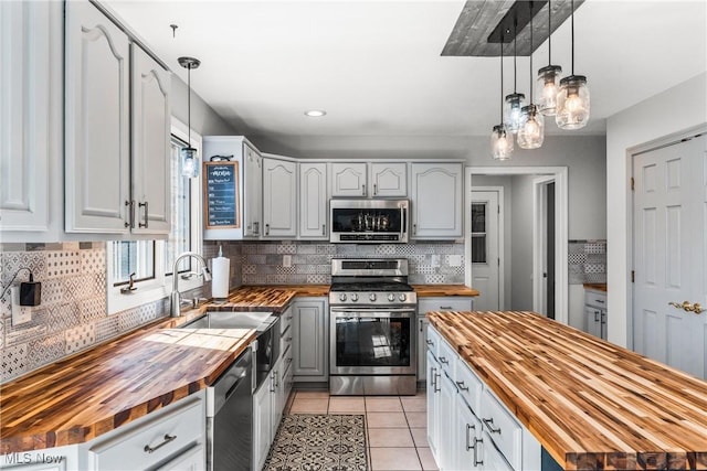 kitchen featuring butcher block counters, decorative backsplash, light tile patterned flooring, stainless steel appliances, and a sink