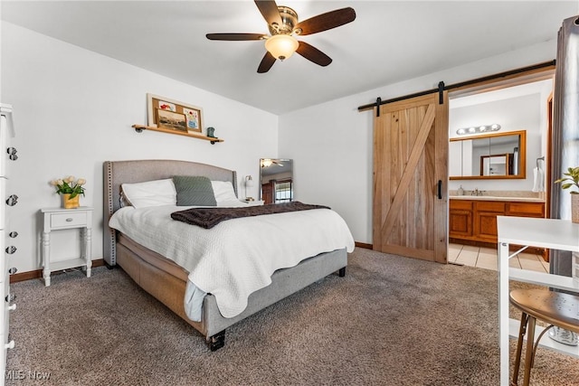 bedroom with baseboards, ceiling fan, a barn door, light carpet, and ensuite bath