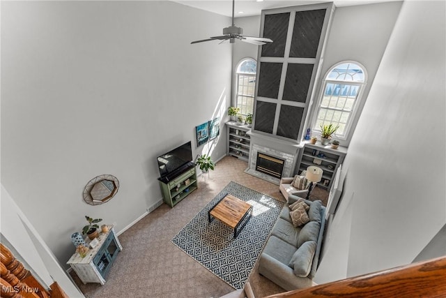 living area featuring baseboards, carpet floors, a premium fireplace, a towering ceiling, and a ceiling fan