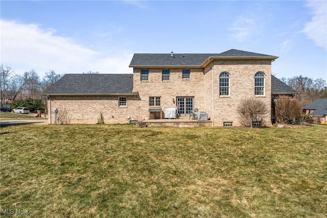 back of property with a yard, brick siding, and roof with shingles