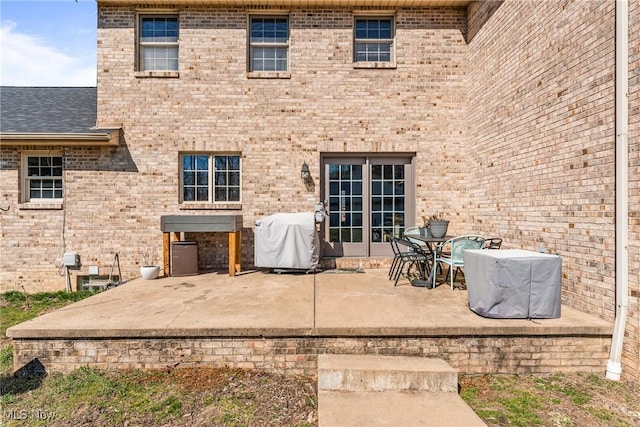 back of property with a patio, brick siding, and roof with shingles