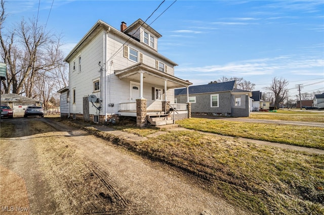 american foursquare style home featuring a front lawn, covered porch, and a chimney