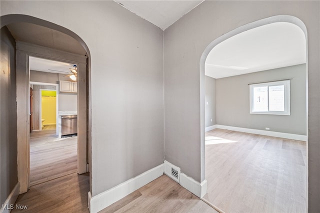 spare room featuring visible vents, arched walkways, baseboards, and wood finished floors