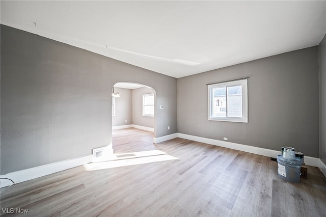 spare room with arched walkways, plenty of natural light, and wood finished floors